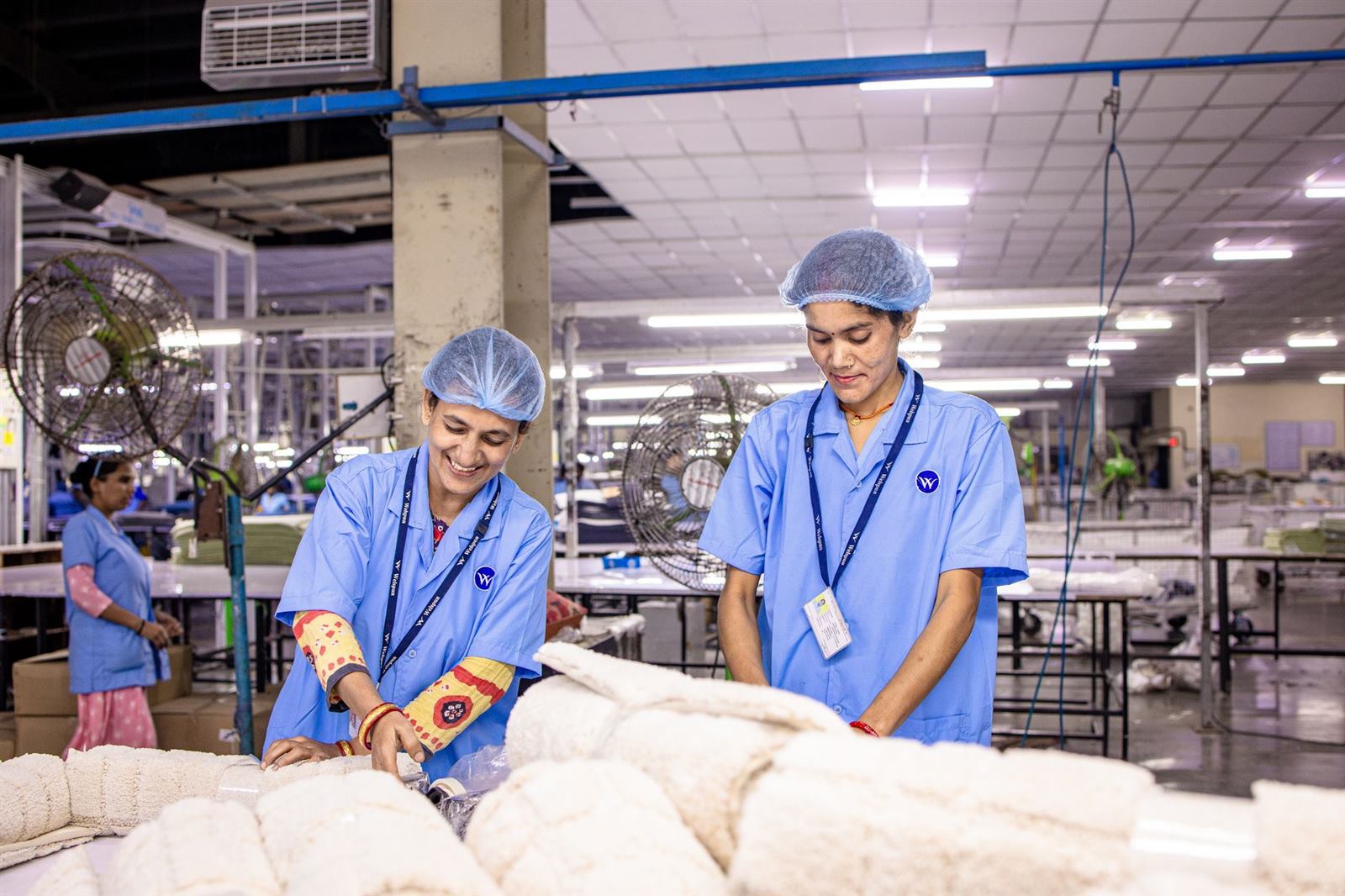Smiling Indian factory workers in a textile factory wearing blue uniforms and hairnets, wo